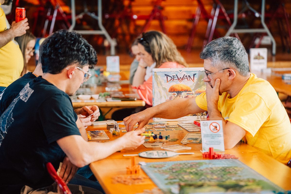 Des joueurs concentrés autour d'une partie de société, plateau et cartes étalés sur la table